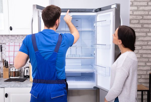 Young Woman Looking At Male Serviceman Checking Temperature Of Refrigerator